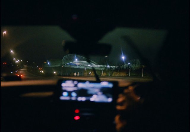 Video Reference: night, car interior, driving, road, street lights, building, city, blurred, low light, windshield, dashboard, urban, transportation, nighttime, out of focus