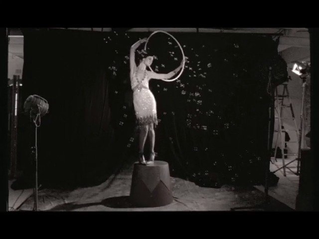 Video Reference: black and white, studio, woman, hoop, bubbles, confetti, performance, pedestal, dark backdrop, fashion, vintage, pose, theater, artistic, indoor, set