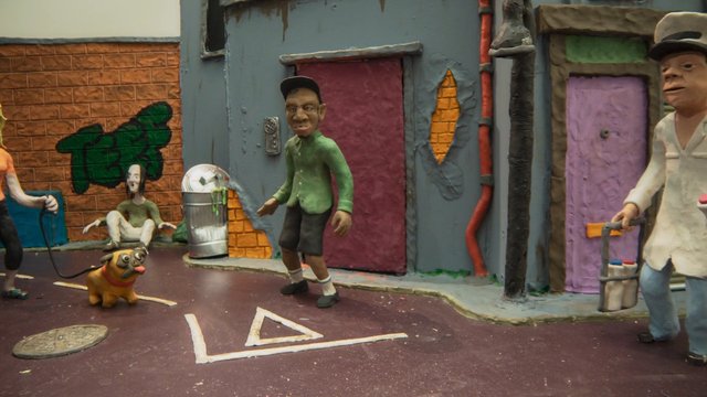 Video Reference: stop-motion, street scene, urban alley, puppet figures, dog, graffiti, colorful buildings, trash can, miniature set, cartoonish, outdoor, model animation