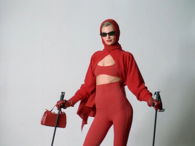 Video Reference: fashion, model, red outfit, sunglasses, headscarf, gloves, ski poles, handbag, studio, posing, minimal background, glamour, runway style, red clothing