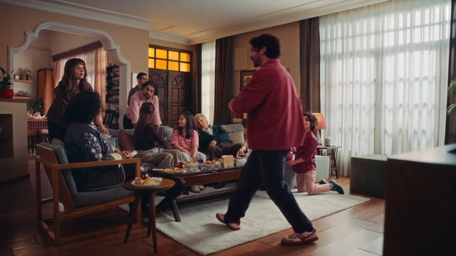Video Reference: living room, family gathering, indoor, conversation, sofa, coffee table, snacks, home interior, people, standing, seated, window, daylight, warm lighting, casual, social