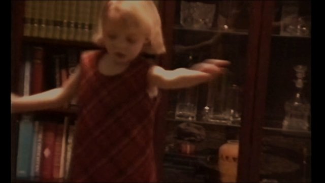 Video Reference: child, toddler, indoor, bookshelf, cabinet, glassware, red dress, motion blur, home interior, standing, arms outstretched, portrait