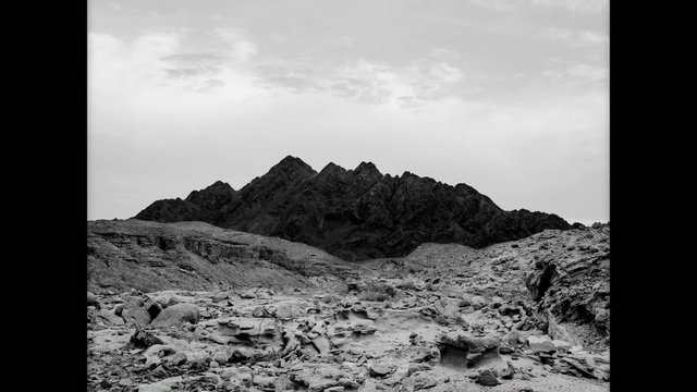 Video Reference: black and white, landscape, desert, rocks, mountains, ridge, cloudy sky, arid, wilderness, terrain, hills, outdoors, nature, rocky ground