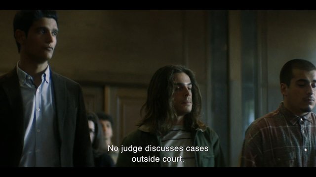 Video Reference: men, indoor, group, dimly lit, room, standing, subtitles, drama, serious, conversation, low light, casual clothing