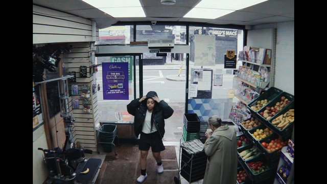 Video Reference: convenience store, market, interior, produce, fruits, vegetables, magazines, doorway, people, shopping, shelves, signs, street view, small shop, retail, casual