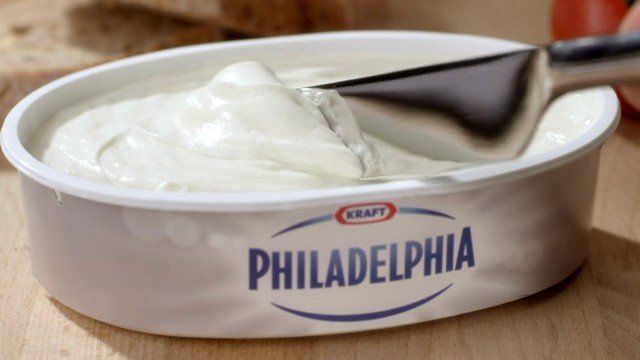 Video Reference: spread, cream cheese, container, spoon, close-up, food, dairy, snack, spreadable, white, wooden table, open tub, product shot