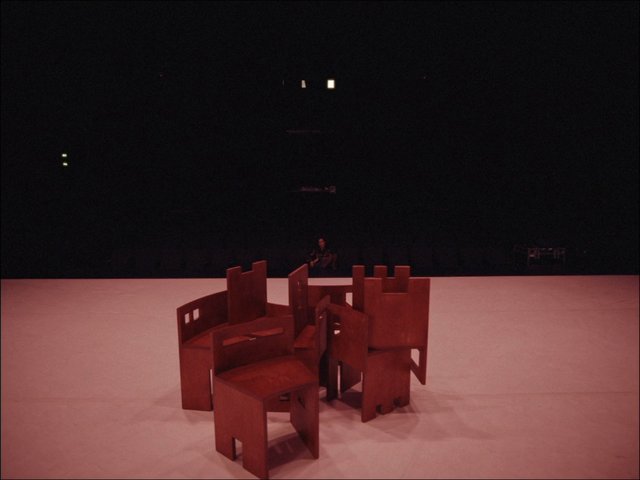 Video Reference: gallery, art installation, sculpture, chairs, wooden, stage, dark background, indoor, minimal, abstract, exhibition, contemporary art