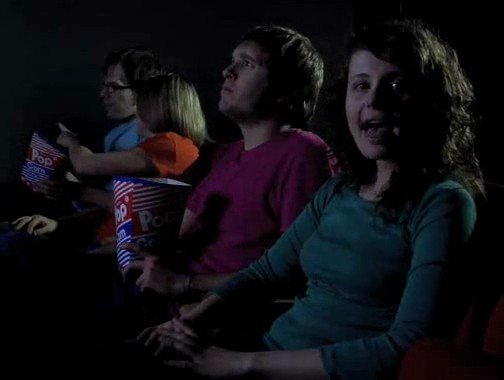 Video Reference: movie theater, audience, popcorn, people, cinema, seated, dark interior, watching film, group, foreground subject, casual, indoor, entertainment