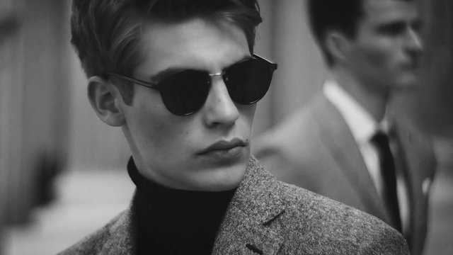 Video Reference: black_and_white, portrait, man, sunglasses, blazer, turtleneck, close_up, fashion, stylish, blurred_background, male, formal, elegant, indoors, monochrome