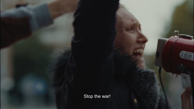 Video Reference: woman, protest, shouting, raised arm, siren, loudspeaker, close-up, outdoor, blurred, subtitle, conflict, demonstration, emotion, activism