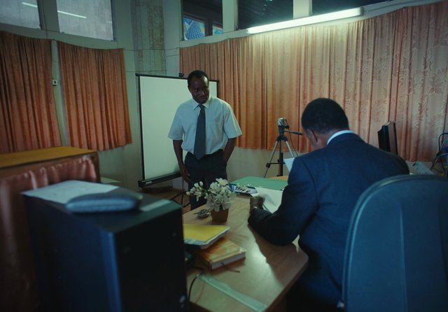 Video Reference: office, meeting, business, men, desk, papers, projection screen, tripod, camera, curtains, chair, books, folders, interview, conference room, indoors