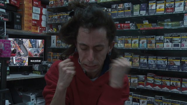 Video Reference: person, tobacco shop, cigarette packs, retail interior, smoke shop, red sweatshirt, store shelves, indoor, portrait, hands raised, tobacco products, commercial interior