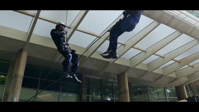 Video Reference: tactical gear, rope, rappelling, suspended, building exterior, glass facade, canopy, action scene, helmet, boots, urban, security, climbing, outdoor, high angle, stunt