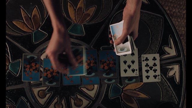 Video Reference: playing cards, card game, hands, tabletop, top view, card layout, deck, gambling, strategy, patterned surface, indoor, close-up, shuffle, deal, game
