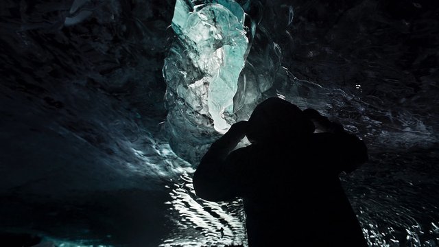 Video Reference: ice cave, silhouette, person, tunnel, glacier, water, reflection, dark, blue ice, adventure, exploration, cold, nature, cavern, dramatic lighting