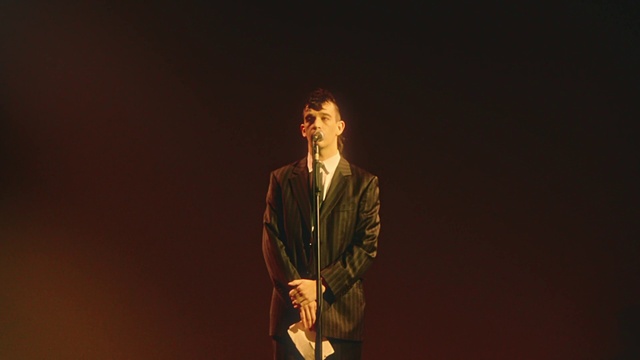 Video Reference: Hand, Sleeve, Flash photography, Entertainment, Blazer, Fashion design, Suit, Performing arts, Formal wear, Audio equipment