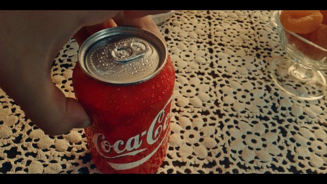 Video Reference: soda can, hand, lace tablecloth, beverage, red can, close-up, table, glass dish, oranges, indoor, still life