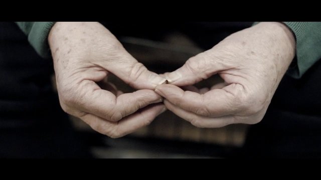 Video Reference: hands, close-up, older adult, holding, pinching, small object, fingers, gesture, dark background, indoor