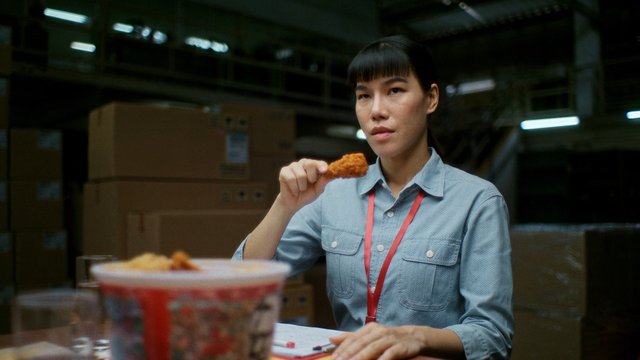 Video Reference: woman, warehouse, stockroom, boxes, fried chicken, table, indoor, workplace, uniform, lanyard, food, storage, office, factory, candid, close-up