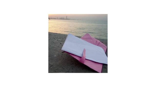 Video Reference: beach, sunset, water, shoreline, paper, envelopes, pink, white, city skyline, calm sea, outdoors, coastal, still life, evening, travel