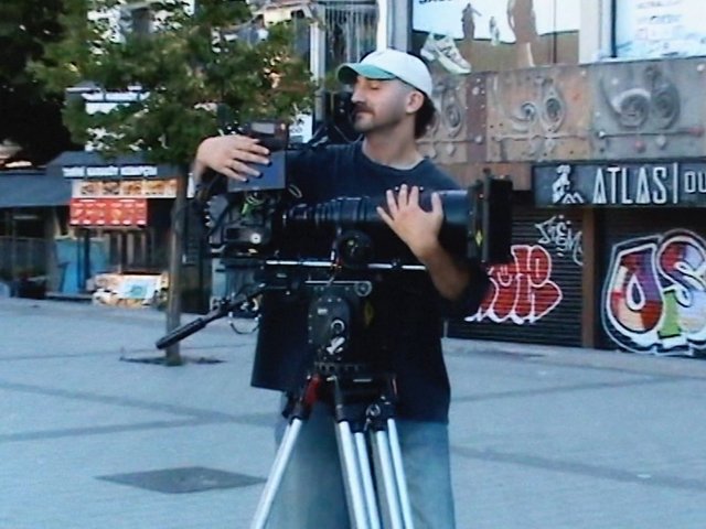 Video Reference: man, camera, tripod, videographer, filmmaking, outdoor, urban, graffiti, street, equipment, crew, production, cinematography, cap, daylight