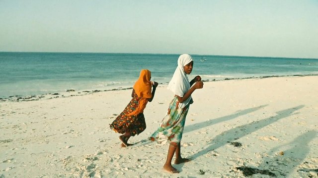 Video Reference: beach, girls, walking, sand, sea, ocean, headscarf, barefoot, shoreline, outdoors, daylight, tropical, coast, children, summer