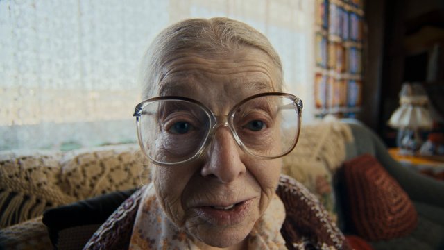 Video Reference: elderly woman, close-up, glasses, indoor, living room, portrait, senior, couch, home interior, face, bokeh, soft light