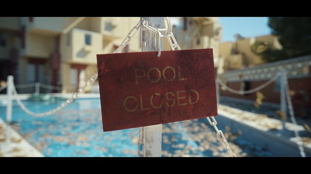 Video Reference: pool, closed, sign, chain, swimming pool, fence, outdoors, apartment buildings, water, sunny, blurry background, restricted area