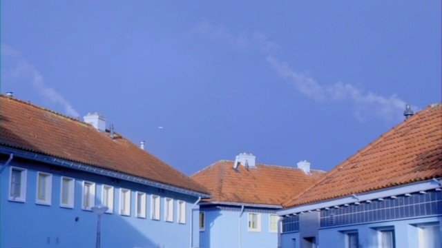 Video Reference: buildings, residential, rooftops, tiled roof, blue facade, sky, outdoor, architecture, neighborhood, sunny, daylight, windows, courtyard, urban, houses
