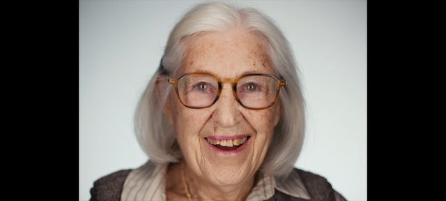 Video Reference: elderly woman, portrait, close-up, smiling, gray hair, glasses, face, studio background, headshot, portrait photo