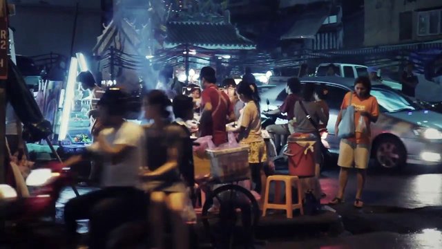 Video Reference: night market, street food, crowd, vendors, scooters, cars, street scene, nighttime, wet road, urban, outdoor, traffic, market stall, people, lights, Thailand