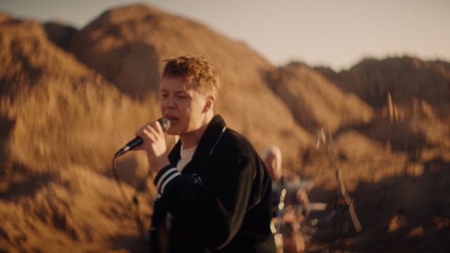 Video Reference: Microphone, Shirt, Mountain, Flash photography, Music, Musician, Landscape, Sky, Audio equipment, Event