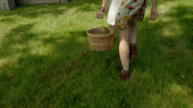 Video Reference: person, walking, grass, yard, bucket, wooden bucket, floral dress, outdoors, garden, summer, back view, legs, handheld, daylight