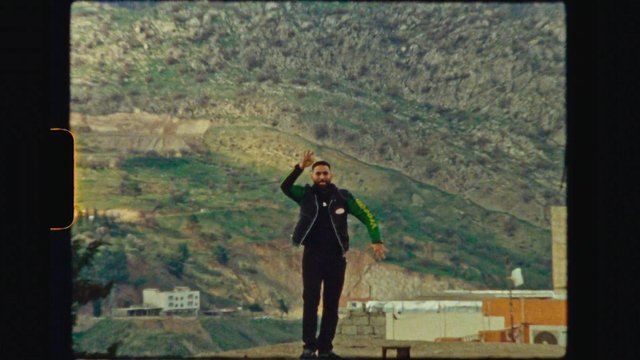 Video Reference: man, outdoors, hillside, mountains, landscape, standing, waving, portrait, travel, nature, village, rocky, scenic, person