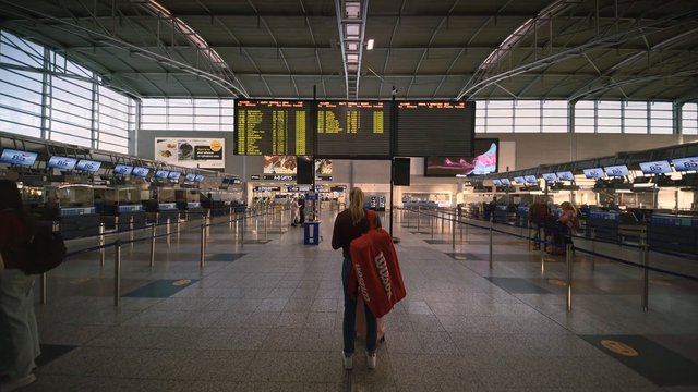 Video Reference: airport, terminal, check-in, departure board, travel, indoor, hall, queue, passengers, transit, wide shot, travelers, information display, architecture