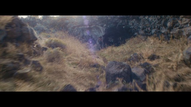 Video Reference: rocky landscape, cave entrance, dry grass, hillside, outdoor, person, nature, rural, rocks, sunlight, trail, wilderness