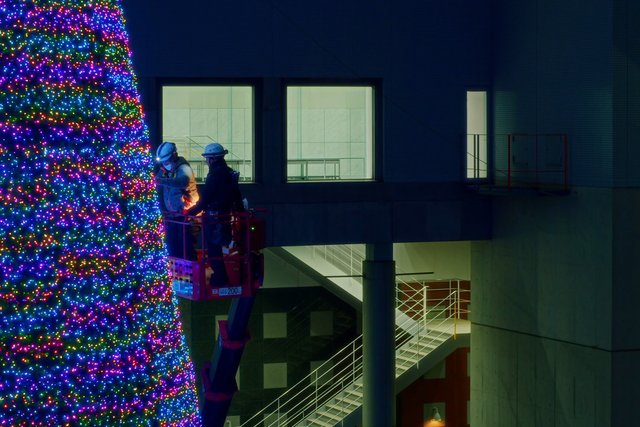Video Reference: workers, lift platform, LED lights, holiday lights, building exterior, night, installation, construction, multicolored, illumination, window, stairs, indoor atrium, maintenance