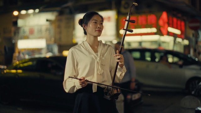 Video Reference: woman, street, night, city, music, musician, traditional instrument, bowed string instrument, performance, neon lights, urban, outdoor, portrait, cultural, evening, blurred background