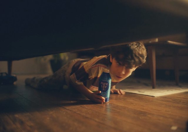 Video Reference: child, crawling, floor, indoors, water bottle, furniture, low angle, dim light, wooden floor, home, playful, bottle, under table, boy