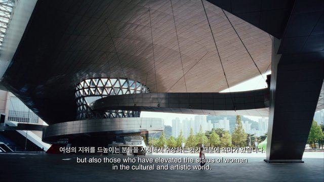 Video Reference: modern architecture, plaza, urban, curved structure, metal facade, city skyline, outdoor, public space, contemporary building, architecture, subtitles, bilingual text, daylight, landmark