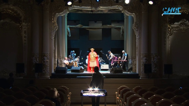 Video Reference: Musical instrument accessory, Dress, Building, Entertainment, Chair, Performing arts, Curtain, Suit, Music venue, Event