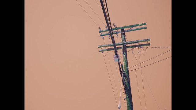 Video Reference: utility pole, power lines, telephone pole, overhead wires, electricity, sky, orange sky, haze, outdoors, industrial, cables, street infrastructure