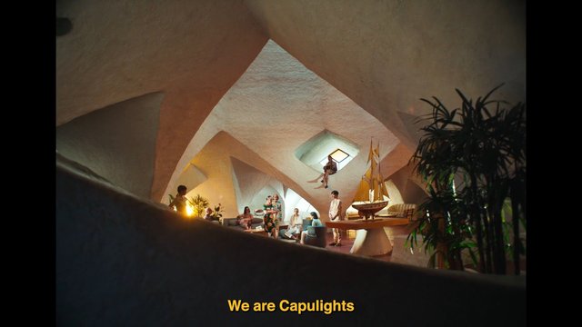 Video Reference: indoor, lounge, group of people, modern interior, sculptural architecture, plants, sofa, table, model sailboat, warm lighting, art installation, contemporary design, text overlay, decorative