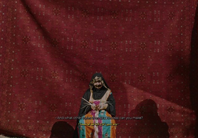 Video Reference: person, traditional clothing, textile, patterned backdrop, red fabric, cultural scene, portrait, stage, subtitles, indoor, costume, handmade, craft, fabric art