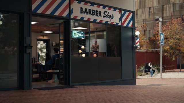 Video Reference: barber shop, storefront, neon sign, open sign, city plaza, sidewalk, window display, interior, customer, street scene, urban, daytime, chairs, people