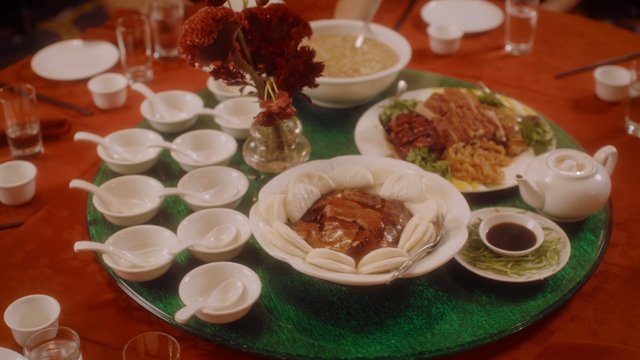 Video Reference: banquet, dining table, Chinese food, feast, table setting, teapot, bowls, cups, centerpiece, restaurant, shared meal, catering, dinner, food spread