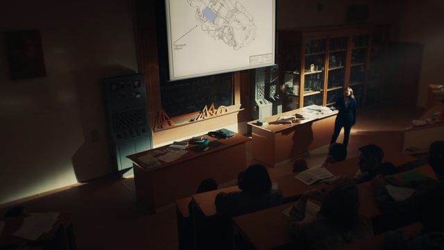 Video Reference: Table, Chair, Desk, Building, Projection screen, Event, Space, Suit, Conference hall, Display device