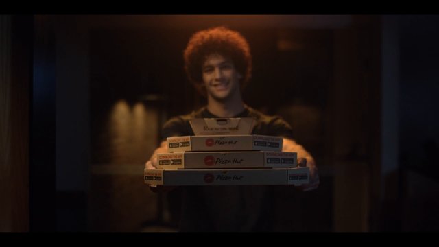 Video Reference: man, pizza boxes, delivery, indoor, smiling, warm light, food, takeout, stacked boxes, restaurant, advertising, close-up, casual, young adult