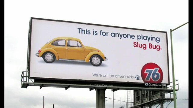 Video Reference: billboard, advertisement, car, beetle, volkswagen, roadside, outdoor, signage, yellow car, classic car, text, logo, sky, urban, marketing