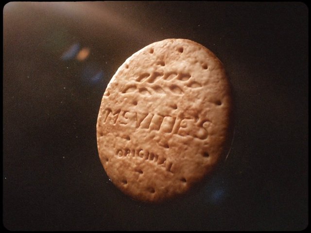 Video Reference: biscuit, cookie, snack, close-up, food, round, textured, embossed, brown, dark background, macro, studio, single object